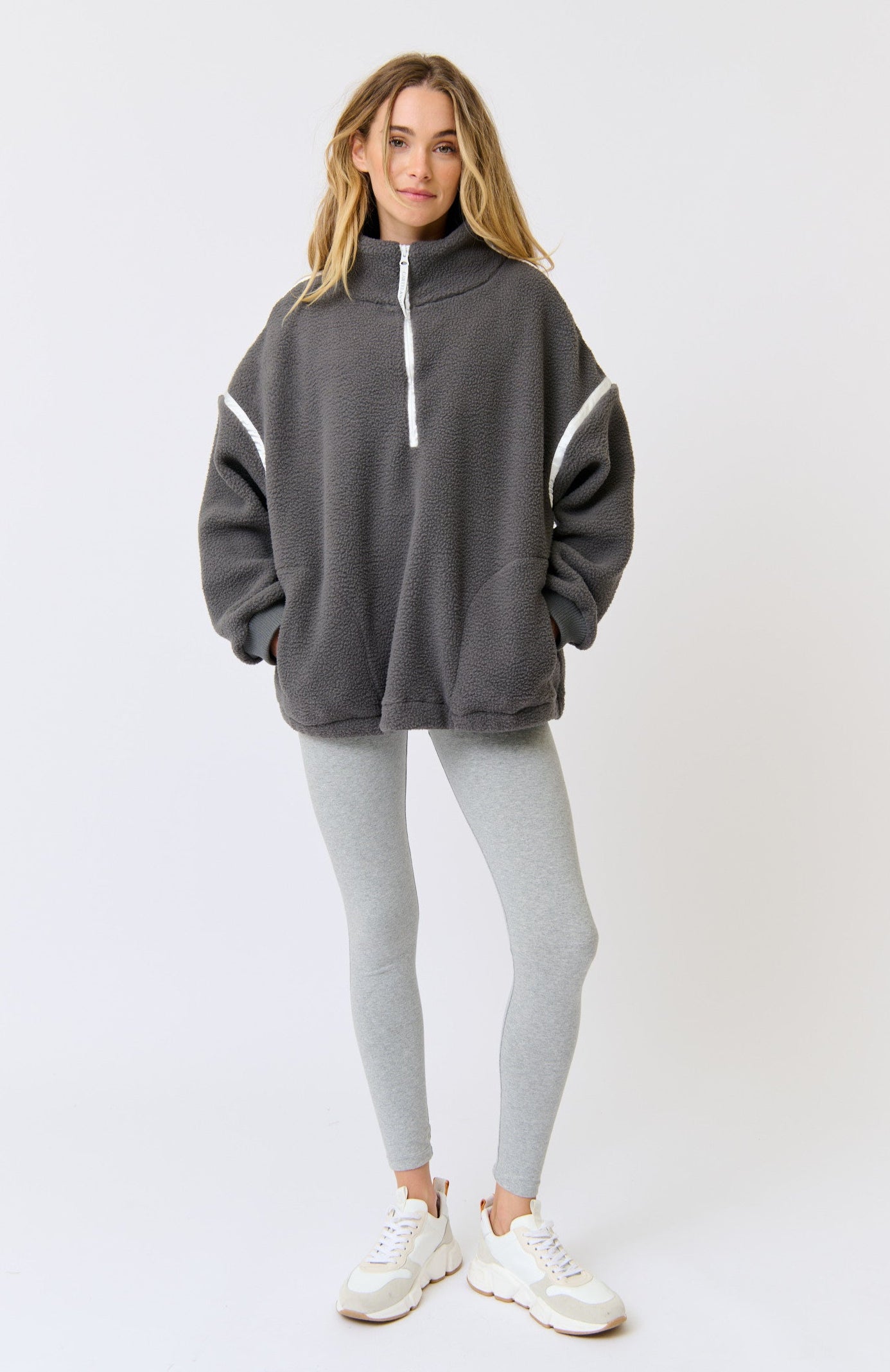 Woman wearing a gray hoodie with white accents and leggings on a white background