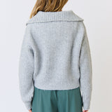 Person wearing a light gray knitted cardigan and green pants on a white background