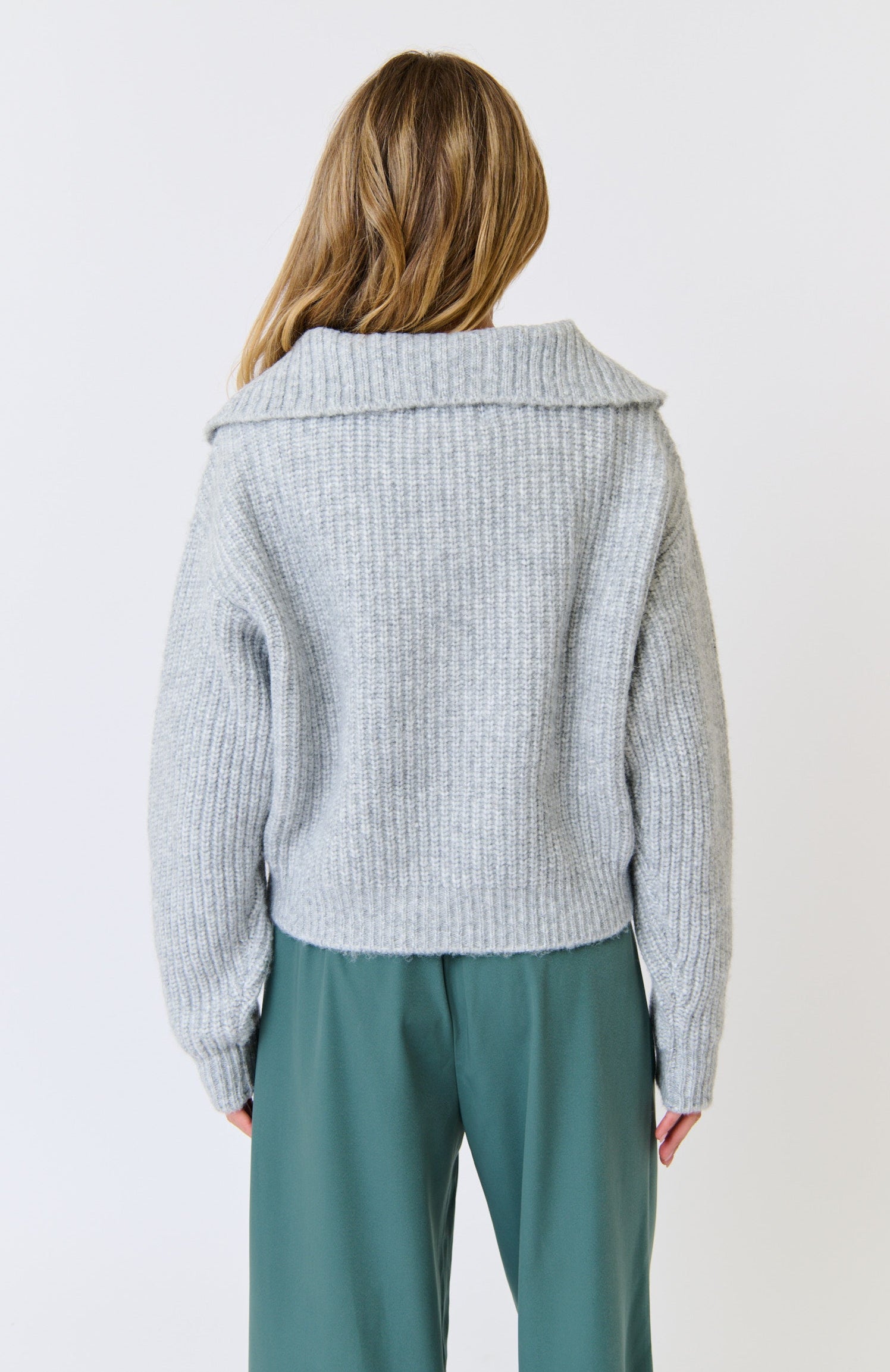 Person wearing a light gray knitted cardigan and green pants on a white background